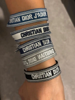 Dior armband - Säljer flera snygga broderade armband från Christian Dior i olika nyanser av blått, grått och svart. Armbanden har tydlig logga, justerbar knytning med tofsar och är tillverkade i textil. Perfekt accessoar för att lyfta din outfit.