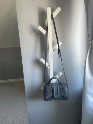 Grå fluffig handväska med axelrem - Säljer en snygg grå handväska med fluffig teddystruktur och matchande detaljer i konstläder. Väskan har både handtag och justerbar axelrem i samma färg. Stängs med ett lock framtill och har guldfärgade metalldetaljer. Perfekt för dig som gillar trendiga accessoarer. Buda gärna!!!