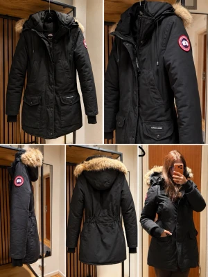 Canada Goose Jacka  - Svart parkasjacka från Canada Goose med klassisk patch på ärmen och fuskpäls på huvan. Jackan har dragkedja, stora fickor framtill och justerbar huva. Storlek XS, justerbar i midjan. 