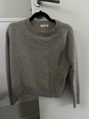 Grå beige stickad tröja från Soft Goat - Mysig grå stickad tröja från Soft Goat i klassisk modell med rund halsringning och ribbade muddar. Tröjan är tillverkad i ett mjukt cashmere utan någon moppen som ger en avslappnad och stilren look. Perfekt för kyliga dagar.❤️