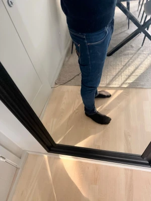Nudie jeans Mörkblåa - Säljer ett par mörkblå nudie jeans med klassisk femficksdesign och dragkedjegylf. Jeansen har smal passform och sitter snyggt längs benen. Perfekta för dig som gillar en modern och stilren look.