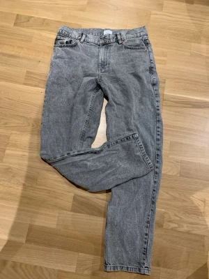 Grå tvättade Grunt jeans - Säljer ett par grå tvättade jeans med rak passform och klassisk femficksdesign. Jeansen har hög midja och är tillverkade i ett robust denimtyg. Perfekta för dig som gillar en avslappnad och vintageinspirerad stil.