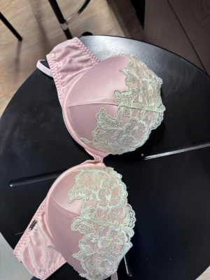 Rosa bh med spetsdetaljer - Snygg rosa  bh med vadderade kupor och ljusbeige spetsbrodyr över kuporna. Axelbanden är justerbara och bh:n har hakknäppning bak. Materialet är glansigt och ger en lyxig känsla. Perfekt för dig som vill ha något extra fint under kläderna. Bra skick i stl 80B. Nypris 449kr. Bara att höra av dig vid frågor eller vid fler bilder!💞