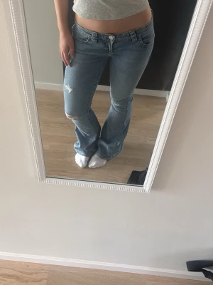 Ljusblå bootcut jeans med slitning - Säljer ett par lågmidjade ljusblå bootcut jeans med slitning och detaljer på bakfickorna. 