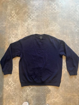 Mörkblå loose fit sweatshirt H&M - En enkel och stilren mörkblå sweatshirt från H&M i loose fit-modell. Tröjan har rund halsringning, ribbade muddar vid ärmslut och nederkant samt är tillverkad i mjuk bomull. Perfekt för en avslappnad och bekväm stil.