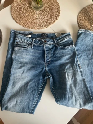 Blå raka jeans med tvättad look från Jack and Jones  - Säljer ett par klassiska blå jeans med rak passform och snyggt tvättad finish. Jeansen har fem fickor, bälteshällor och knappgylf. Perfekta till vardags för en avslappnad stil. Materialet är denim i bomull. Dem är inte mycket använda och dem är storlek 29/32. Hör av dig vid frågor! Kan gå ner i pris vid snabb affär