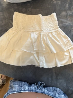 Vit volangkjol med smock - Supersöt vit kortkjol med bred smock i midjan och dubbla volanger. Kjolen är lätt och luftig, perfekt för varma dagar. Pris kan diskuteras