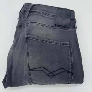Replay svarta jeans straight fit - Svarta jeans från Replay med diskret tvättad look och raka ben. Klassisk femficksmodell med snygga detaljer på bakfickorna och svart patch i midjan. Jeansen är i stretchigt denim som sitter skönt och passar till allt. Det är sytt inuti fickorna.