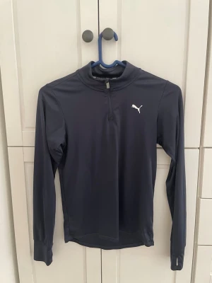 Mörkblå träningströja från Puma - Snygg mörkblå långärmad träningströja från Puma med halv dragkedja och vit logga på bröstet. Tillverkad i ett stretchigt funktionsmaterial som passar perfekt till träning eller löpning. Träningstopparna är 80kr/st