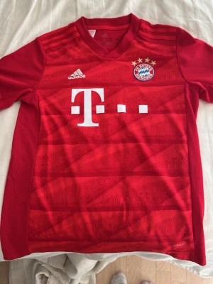 Röd FC Bayern München matchtröja - Säljer en röd FC Bayern München matchtröja från säsongen 19/20. Tröjan har vita detaljer, Adidas-logga och Telekoms sponsortryck. Tillverkad i lätt och ventilerande material, perfekt för fotboll eller träning. Tröjan är i storlek M (barnstorlek) och passar ca 11-12 år. Tröjan är använd någon gång och är i väldigt bra skick.