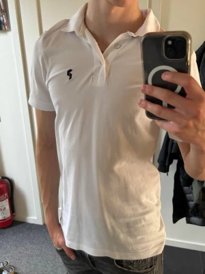 Peak Performamce Vit Piké - Klassisk vit pikétröja med krage och korta ärmar. Tröjan har knappar framtill och en liten svart logga på bröstet. Perfekt för en clean och stilren look. Tillverkad i mjukt bomullsmaterial som känns skönt mot huden. Hör av dig vid frågor!