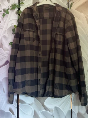 Oversized rutig skjorta i svart och beige - Stilren oversized skjorta med stora rutor i svart och beige. Skjortan har två bröstfickor med knapp, klassisk krage och knäppning framtill. Perfekt för en avslappnad look och enkel att styla lager på lager.