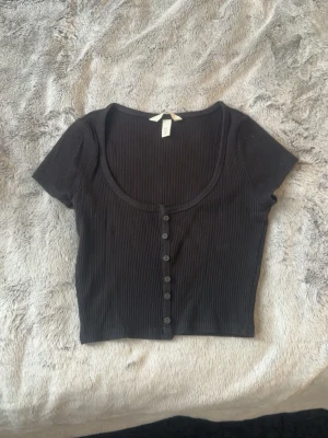 Svart croppad ribbad topp - Snygg svart croppad topp med ribbad struktur och knappar framtill.