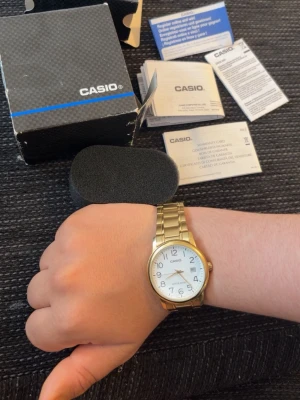 Casio guldfärgad klocka med länkarmband - Stilren klocka från Casio med guldfärgat länkarmband och vit urtavla. Klockan har tydliga svarta siffror, datumvisning och klassisk rund form. Perfekt accessoar för dig som gillar enkel och tidlös design. Pris kan diskuteras