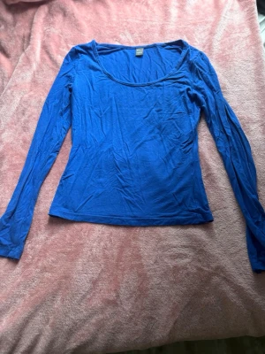 Kornblå långärmad topp - En enkel och stilren kornblå långärmad topp med rund halsringning. Toppen har en slim passform och är tillverkad i ett mjukt och stretchigt material som känns skönt mot huden. Perfekt att matcha med jeans eller kjol. Har använt den 3 gånger!