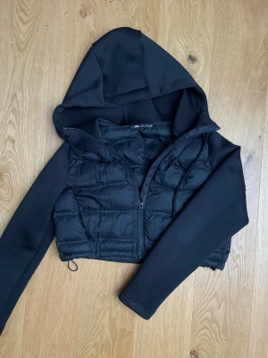 Svart cropped pufferjacka från ZARA - Snygg svart cropped pufferjacka från ZARA med huva och dragkedja framtill. Jackan har vadderad kropp och släta ärmar, samt dragsko i nederkant för justerbar passform. Den har också bra innerfickor med mycket plats (bild 4) Knappast använd. Funka bra till hösten då den är varm fast croopad  original pris runt 300kr