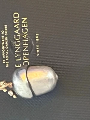 Halsband med ekollonberlock från Ole Lynggaard big size 1600us dollar nypris  - Unikt halsband från Ole Lynggaard med en ekollonformad berlock i silver och detaljer i guld. Berlocken har en organisk, handgjord känsla och hänger i en ögla med små gulddetaljer. Perfekt för dig som gillar naturinspirerade smycken.