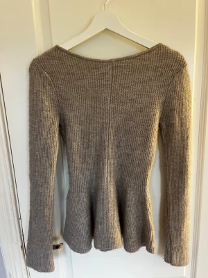 Beige ribbstickad tröja med utsvängd midja - En beige ribbstickad tröja med lång ärm och lätt utsvängd midja. Tröjan har en enkel, klassisk design med rund halsringning och är stickad i ett mjukt material som känns skönt mot huden. Använd 1 gång.