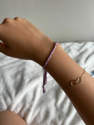Lila flätat armband i bomull - Säljer ett lila och vitt flätat armband i bomullssnöre. Armbandet har justerbar knut och justerbar. Perfekt för att addera lite färg till din outfit.💕
