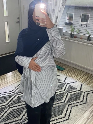 Vit skjorta med svarta ränder och knyt - Säljer en oversized vit skjorta med tunna svarta ränder och en snygg knytning i midjan. Skjortan har långa ärmar och klassisk krage. Perfekt för dig som gillar en relaxed och trendig stil.