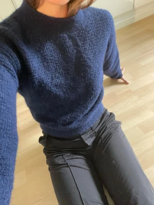 Mörkblå stickad tröja med hög hals - Mysig mörkblå stickad tröja med hög hals och lång ärm. Tröjan har en enkel, klassisk design och är gjord i ett mjukt, fluffigt material som känns skönt mot huden. 
