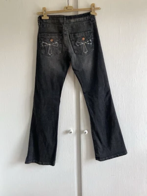 Svarta bootcut jeans med broderi från gina - Snygga svarta bootcut low waist jeans med lätt tvättad look och broderade detaljer på bakfickorna. Jeansen har klassisk femficksmodell och stängs med knapp och dragkedja. Materialet är denim i bomull. Mycket bra skick!💞