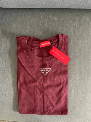Vinröd t-shirt från  - Snygg vinröd t-shirt från med klassisk rund halsringning och broderad logga framtill. Tillverkad i mjuk bomull som känns skön mot huden. Perfekt för dig som vill ha en stilren och trendig look.