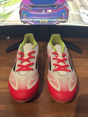 Adidas f50 club fotbollsskor  - Säljer ett par snygga Adidas fotbollsskor i vitt och rött med svarta ränder på sidorna och limegröna detaljer vid öppningen. Använda fåtal gånger.  Skorna har röda snören och är designade för bra grepp på planen. Perfekta för dig som vill sticka ut på matchen!