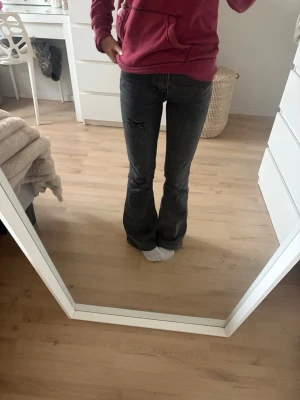 Grå bootcut jeans med slitningar - Säljer ett par grå bootcut jeans med coola slitningar på låret och på ena knät. Jeansen har klassisk femficksdesign och är i ett mjukt denimtyg.💞
