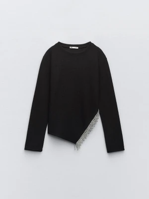 Svart stickad tröja med pärldetalj - Trendig svart stickad tröja från Zara med lång ärm och rund halsringning. Tröjan har en asymmetrisk nederkant dekorerad med glittrande pärlor och stenar som ger en unik touch. Perfekt för dig som vill sticka ut lite extra.
