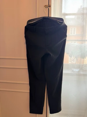 Svarta kostymbyxor från Plain Units - Snygga svarta kostymbyxor från Plain Units med rak passform och klassisk midja. Byxorna har diskreta sidfickor och är tillverkade i ett slätt tyg som ger en stilren look. Perfekta för dig som vill ha en clean och modern stil. Saknas en knapp.