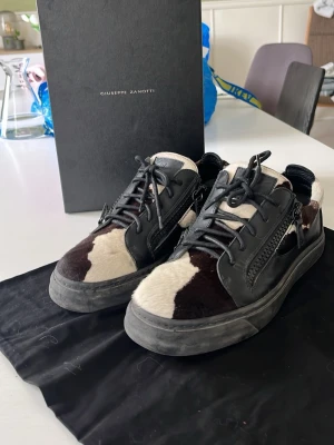 Giuseppe Zanotti sneakers med pälsdetaljer - Unika sneakers från Giuseppe Zanotti med svart och vit pälsdetalj, svarta läderpaneler och dragkedjor på sidorna. Skorna har en chunky svart sula och snörning framtill. Perfekt för dig som vill sticka ut med en cool och lyxig look. Pris är diskuterbart. 