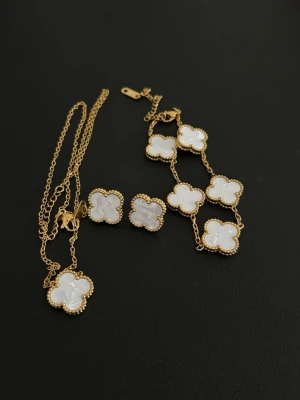 Guldhalsband med vita fyrklöver - Snyggt halsband i guldton med flera vita fyrklöverformade hängen i pärlemor. Kedjan är tunn och elegant, och varje hänge har en dekorativ guldkant. Perfekt för dig som gillar unika och trendiga smycken med en lyxig touch.