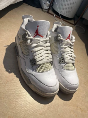 Vita Air Jordan 4 sneakers - Säljer ett par klassiska Air Jordan 4 sneakers i vitt med grå och röda detaljer. Skorna har snörning, meshpaneler och den ikoniska Jumpman-loggan på plösen.       Skick: Fint använt skick! De har lite naturliga veck på tåboxen och lätt gulnad på nätet som det alltid blir på denna modell, men lädret är fint och skorna har mycket liv kvar. Däremot saknas både original kvitto och låda. Men skorna köptes i Sole World, Los Angeles några år tillbaka. 