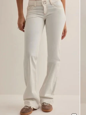 Vita bootcut jeans med kontrastsömmar - Snygga vita bootcut jeans med beige kontrastsömmar och klassiska fem fickor. Jeansen har en hög midja och utsvängda ben, samt dekorativa sömmar på bakfickorna. Perfekta för en trendig och avslappnad look. helt nya jeans med lappen kvar!