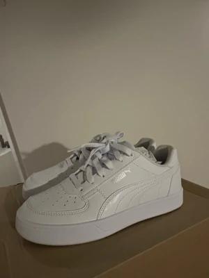 Vita Puma sneakers i läder - Stilrena vita sneakers från Puma i lågt modellutförande. Skorna är tillverkade i slätt läder med klassisk snörning och diskret Puma-logga på sidan. Perfekta för dig som gillar en clean och sportig look. Storlek 38,5. Alldrig andvända, nypris 799:- Pris går att diskutera vid snabb affär.