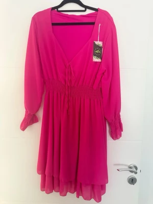 💖✨ Klänning från Mila XL/XXL – ny med etikett ✨💖 - 💖✨ Klänning från Mila XL/XXL – ny med etikett ✨💖  🌸 Vacker klänning från Mila i en intensiv ceriserosa färg. Feminint omlottliv med knytband, smockad midja och en lätt utsvängd, luftig kjol som ger en smickrande passform. Perfekt för bröllop, fest, dop eller andra speciella tillfällen. 💃  💎 Skick: Ny med etikett 🏷️ Märke: Mila 📏 Storlek: XL/XXL  📐 Mått: • Byst: 120 cm (stretch upp till ca 130 cm) • Längd: 93 cm  📩 Hör gärna av dig om du har frågor. Välkommen att köpa! 😊