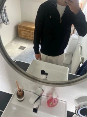Morris halvzip tröja - Snygg svart tröja med halvzip och liten broderad logga på bröstet. Tröjan har ribbade muddar vid ärmslut och nederkant samt hög krage. Perfekt för lager på lager och enkel att matcha med olika outfits.