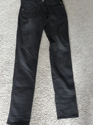 Svarta replay  jeans - Säljer ett par svarta jeans med rak passform och klassisk femficksdesign. Jeansen har knappgylf och bälteshällor, perfekta till en avslappnad stil. 