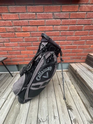 Callaway golfbag svart och grå - Säljer en snygg golfbag från Callaway i svart och grått. Väskan har flera fack, bärrem och praktiska benstöd så den står stadigt på marken. Perfekt för att ta med sig klubborna ut på banan och hålla ordning på utrustningen.