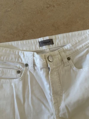 Vita raka jeans från Filippa K - Snygga vita jeans från Filippa K med klassisk femficksmodell och raka ben. Jeansen har silverfärgade nitar och knapp, samt bälteshällor i midjan. Tillverkade i ett mjukt bomullstyg som känns bekvämt och stilrent.