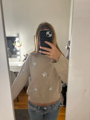 Beige stickad tröja med stjärnor - Säljer en beige stickad tröja med silvriga stjärnor broderade på framsidan. Tröjan har en avslappnad passform, rund halsringning och ribbade muddar vid ärmslut och nederkant. Perfekt för dig som gillar mysiga och trendiga plagg.🤍💛