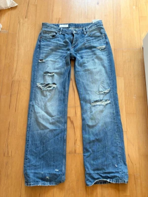 Lågmidjade mörkblå jenas med slitningar från Zara - Säljer ett par trendiga blå jeans med raka ben och flera slitningar och hål på framsidan från Zara. Jeansen är endast använda ett fåtal gånger, väldigt bra skick. I storlek 42, nypris 400kr. Perfekta för en avslappnad och trendig look.❤️🙌