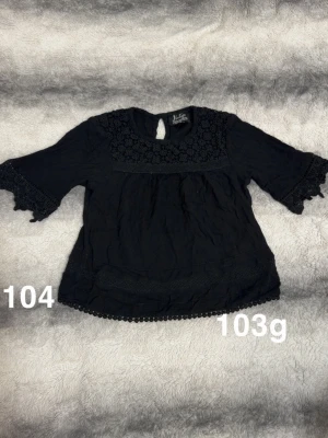 Svart blus med spetsdetaljer - Söt svart blus med trekvartsärm och fina spetsdetaljer vid halsringning och ärmslut. Blusen har en liten knapp i nacken och dekorativ kant längst ner. Perfekt för dig som gillar en romantisk och stilren look.🌸 Fint använt skick. Storlek 104