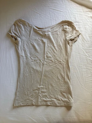 Beige topp med öppen rygg - Snygg beige topp med korta ärmar och en djup, öppen rygg. T-shirten har en figurnära passform och är tillverkad i ett mjukt material som känns skönt mot huden. Perfekt för dig som vill ha en enkel men ändå unik topp.