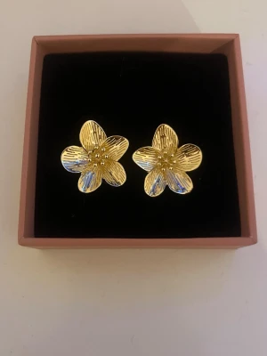 Guldiga blomformade örhängen - Säljer ett par snygga örhängen i form av blommor i guldig färg. Helt nya och oanvända 