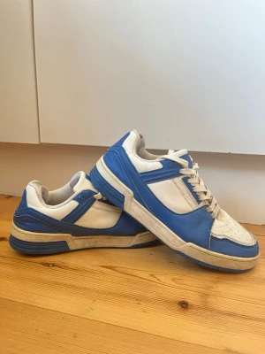 Blåvita sneakers med retrostil från Lejon strl 42 - Snygga sneakers i blått och vitt från Lejon med klassisk retrodesign. Skorna har perforerad tå, vita snören och blå detaljer runt hela skon. Storlek 42.