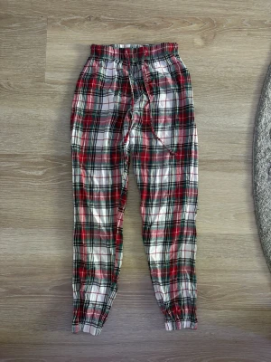 Rutiga pyjamasbyxor xs - Mysiga pyjamasbyxor i rött, vitt och svart rutigt mönster. Byxorna har resår i midjan och dragsko för skön passform samt muddar vid bensluten. I storlek xs, helt rena och inga hål. 