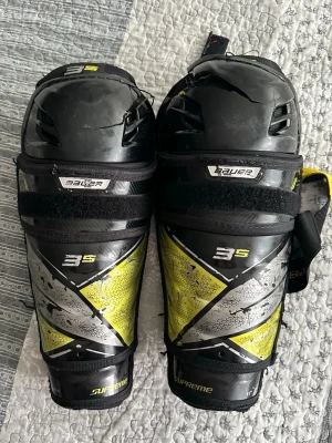 Bauer Supreme 3S benskydd hockey Jr  - Säljer ett par Bauer Supreme 3S benskydd för hockey. Svart och gul design med justerbara kardborreband och vadderad insida för extra komfort och skydd. Perfekta för dig som vill ha bra skydd på isen. Snygg och sportig look!
