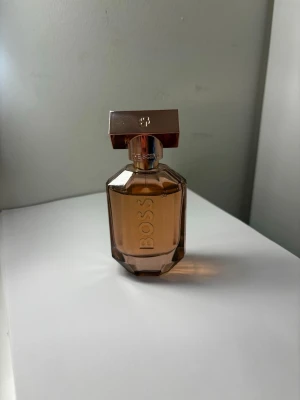 BOSS The Scent parfym brun glasflaska - Elegant parfym från BOSS i en lyxig, facettslipad glasflaska med varm brun ton och metalliskt lock. Flaskan har en modern, geometrisk form och BOSS-loggan ingraverad på framsidan. Perfekt för dig som gillar stilrena och exklusiva dofter. Lita använd, köpte fel doft därav säljer denna